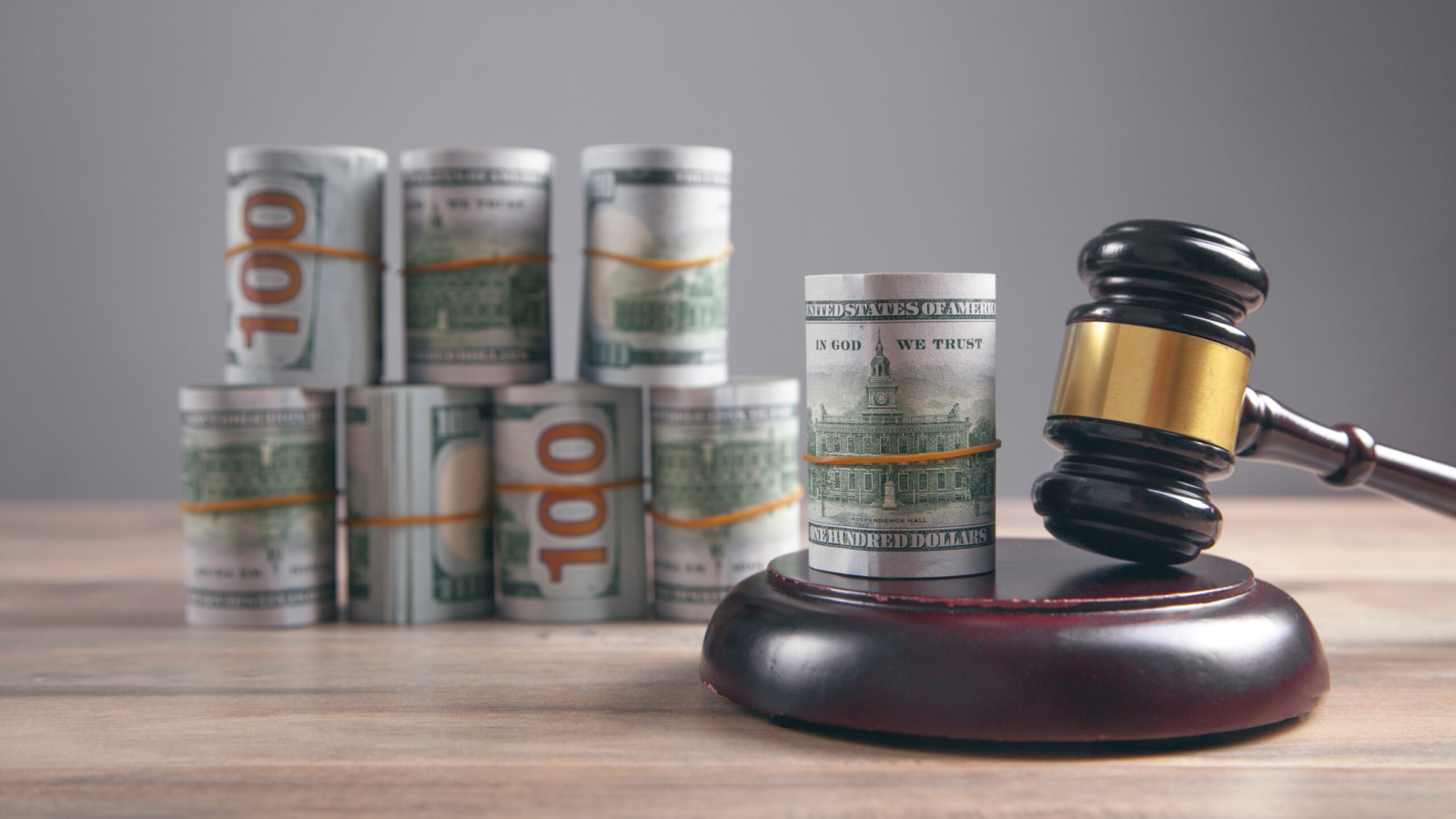 Judge gavel and money rolls on wooden table.
